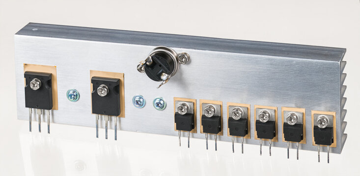 Closeup of electronic components on aluminum heatsink for switched power supply on white background. Bipolar transistors, ultrafast soft recovery diodes and high capacity thermostat screwed on cooler.