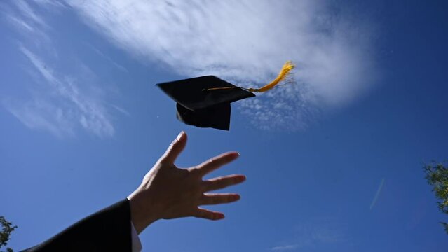 Close-up of a woman's hand throwing a graduation cap into the sky. 