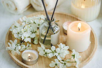 Aroma diffuser, burning candle, cherry blooming flowers and perfume on wooden bamboo tray. Cozy home decor, hygge and aromatherapy concept. Comfortable atmosphere, spring delicious fresh smell