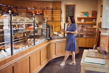 Young pretty woman shopping in a bakery. A customer standing near a showcase with sweets in a store