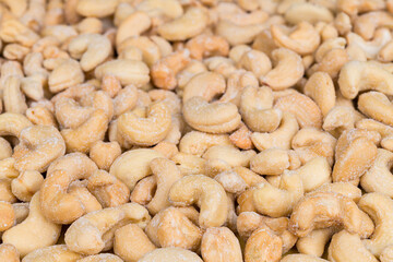 Closeup of yummy salty cashew nuts in culinary background. Anacardium occidentale. Light brown kidney shaped roasted cashews with white salt crystals. Delicious eat in beige texture from edible seeds.