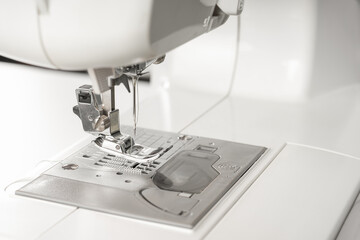 Modern white sewing machine presser foot closeup, macro. Sewing equipment, work tool for atelier business, manufacturing, occupation.