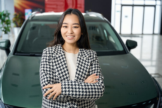 Long-haired brunette stands in front of a sparkling new car
