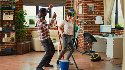 Happy man and woman doing house chores and dancing, listening to music for spring cleaning work....