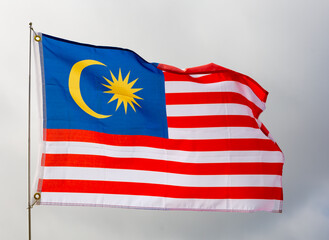 Large flag of Malaysia fixed on metal stick waving against background of cloudy sky during daytime