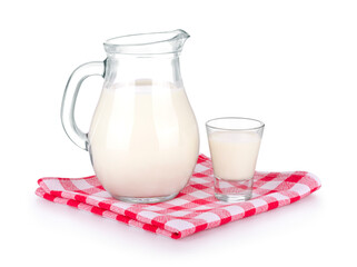A glass of milk and a milk jug on plaid tablecloth.
