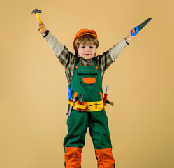 Child in safety helmet and toolbelt with saw and hammer. Work with tools. Boy in builder uniform...