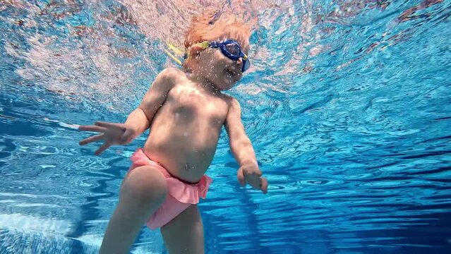 Little cute baby girl, child swimming underwater in swimming pool with water sports instructor, training. Concept of sport, healthy and active lifestyle, childhood, fun and training