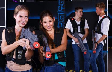Portrait of two cheerful girls with laser guns in their hands in dark laser tag room