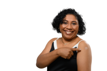 A woman smiles. She points to the vaccine sticker on her arm,