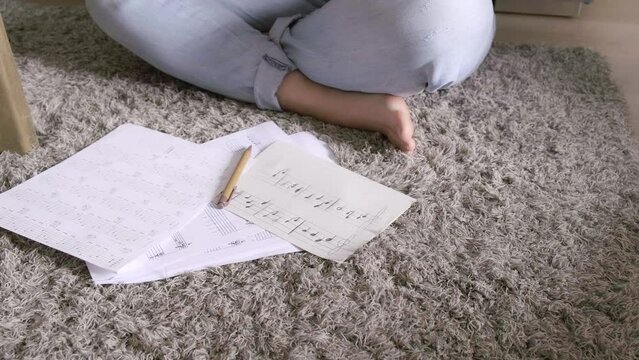 Caucasian woman composing a song sitting with her guitar and some sheet music on the floor of her dining room
