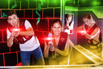 First cheerful person view of young people aiming from laser gun in dark laser tag game room.