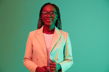 African american woman portrait business smile in glasses on a green background in neon light, colored mixed light, bright colors. Beauty African American woman with pigtails emotions.