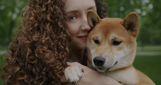 Close-up portrait of beautiful woman holding adorabe shiba inu dog looking at camera on summer day in park. Animal and person concept.