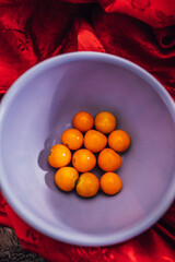 orange colored Golden berries, cape gooseberries in purple, lilac color bowl, red silk backdrop