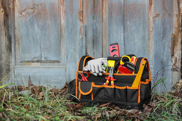 Bag with different tools for repair on grass near wooden door outdoors, space for text