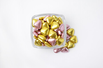 Glass bowl and many delicious heart shaped candies on white background, flat lay