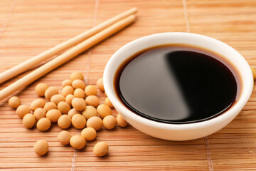 Obraz na płótnie Canvas Soy sauce in bowl and soybeans on bamboo mat, closeup