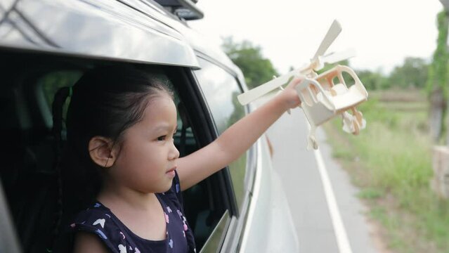 Little girl having fun to play with toy wooden airplane out of car window