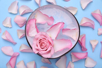 Bowl with water and rose petals on light blue background, flat lay. Spa composition