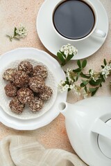 Delicious chocolate candies, cup of hot drink, teapot and blooming branch on beige table, flat lay