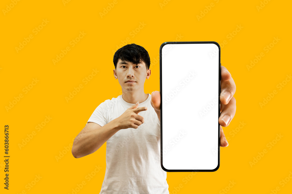 Canvas Prints asian man holding smartphone with white empty screen on yellow background. cellphone display mockup 