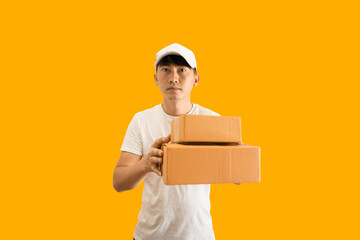 Fototapeta na wymiar Young Asian delivery man wearing cap and white blank t-shirt holding parcel post box isolated on yellow background. express delivery service concept.