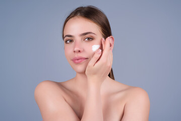 Closeup young woman applying cream to face. Skincare and cosmetics concept. Skin care. Girl applying cream on face on studio background. Skin moisturizer.