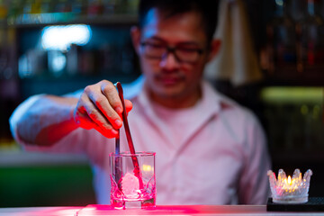 Professional male bartender preparing and serving cocktail drink to customer on bar counter at luxury nightclub. Barman making mixed alcoholic drink for celebrating holiday party at restaurant bar.