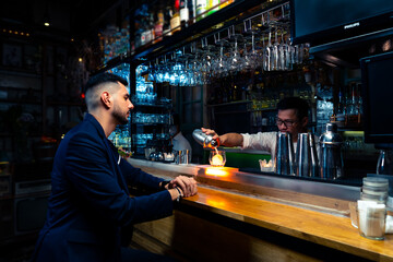 Professional male bartender preparing and serving cocktail drink to customer on bar counter at luxury nightclub. Barman making mixed alcoholic drink for celebrating holiday party at restaurant bar.