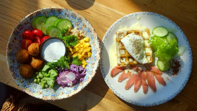 Chickpea falafel salad with vegetables, quinoa and Edamame beans with Zaziki sauce on a wooden table. Healthy vegetarian food. Bright, juicy fresh rations. gluten-free cornmeal waffle with poached egg