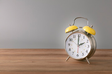 Retro silver alarm clock. 2:00.  am,  pm. Neutral background. Brown wood surface. Horizontal  photography with empty space for text or image.