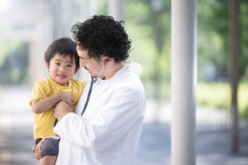 子どもを抱っこする白衣を着た髭の男性小児科医のイメージ　カメラ目線　コピースペースあり