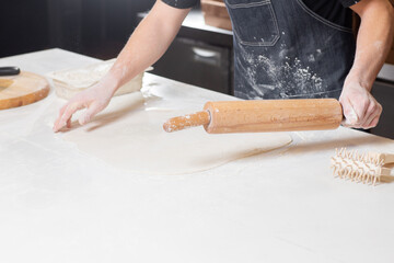 Dough for pizza, the chef rolls out the blanks. Closeup hand of chef baker in uniform white apron cook pizza at kitchen