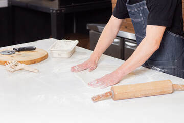 Dough for pizza, the chef rolls out the blanks. Closeup hand of chef baker in uniform white apron cook pizza at kitchen