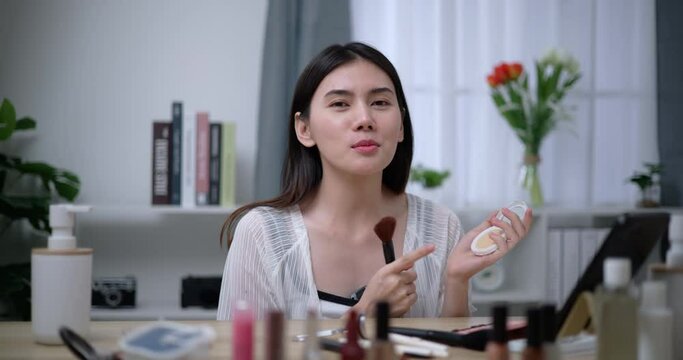 Footage of Beautiful asian woman blogger showing how to make up and use cosmetics. Influencer lady lives streaming cosmetics product reviews in the home studio. Influencer and cosmetics concepts.