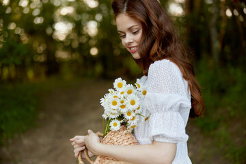 close portrait of a happy, red-haired woman with a wicker basket full of daisies in nature