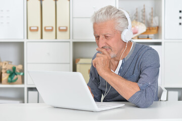 Fototapeta premium Thoughtful old man in headphones with laptop at home