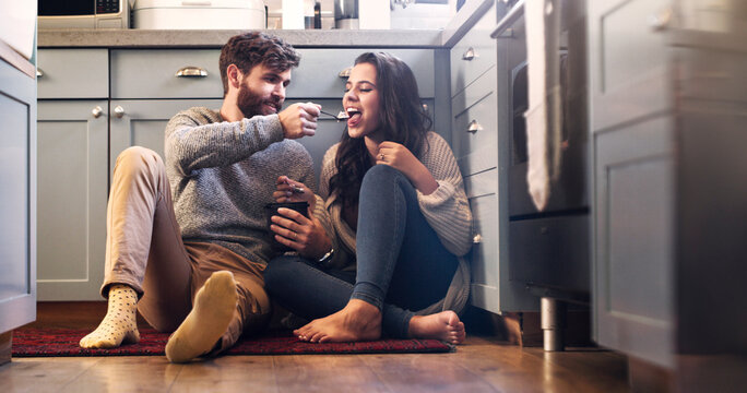 Ice cream, kitchen and couple on floor in home for bonding, relaxing and quality time together. Love, relationship and happy man and woman with sweet treats, dessert and luxury snack for romance