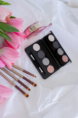 Pink tulips, eye shadow palette with mirror, brushes and perfume bottle on white background, women makeup cosmetics set