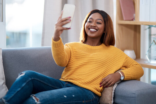 Black woman, happy in selfie and relax on couch in lounge, lifestyle influencer at home and social media post. African female content creator in apartment, smile in picture and communication on app