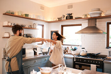 Excited young couple, dance and kitchen in home with love, comic moment and cooking together with...