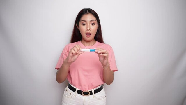 Happy young woman wearing pink shirt showing her pregnancy test in Studio with White background. pregnancy concept