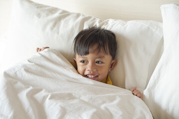 portrait of a smiling boy lying down and wearing a blanket on the bed while watching television