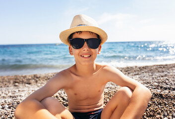 Portrait of a smiling boy on the beach with a straw hat.