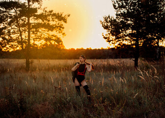 a girl in a black bodysuit stands in a field at sunset