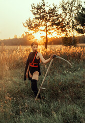 a girl in a black bodysuit stands in a field at sunset