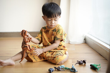 happy handsome asian boy playing with plastic dinosaur toy at home, soft back light