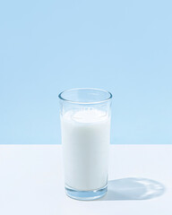 Minimal summer concept of food and drink with glass of milk on pastel blue background. Shadows and sun reflections. Healthy beverages. Dairy source of calcium, protein, vitamins B2, B12 and potassium.
