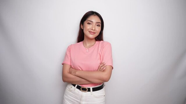 Confident smiling Asian woman dressed in pink, standing with arms folded and looking at the camera in Studio with White background